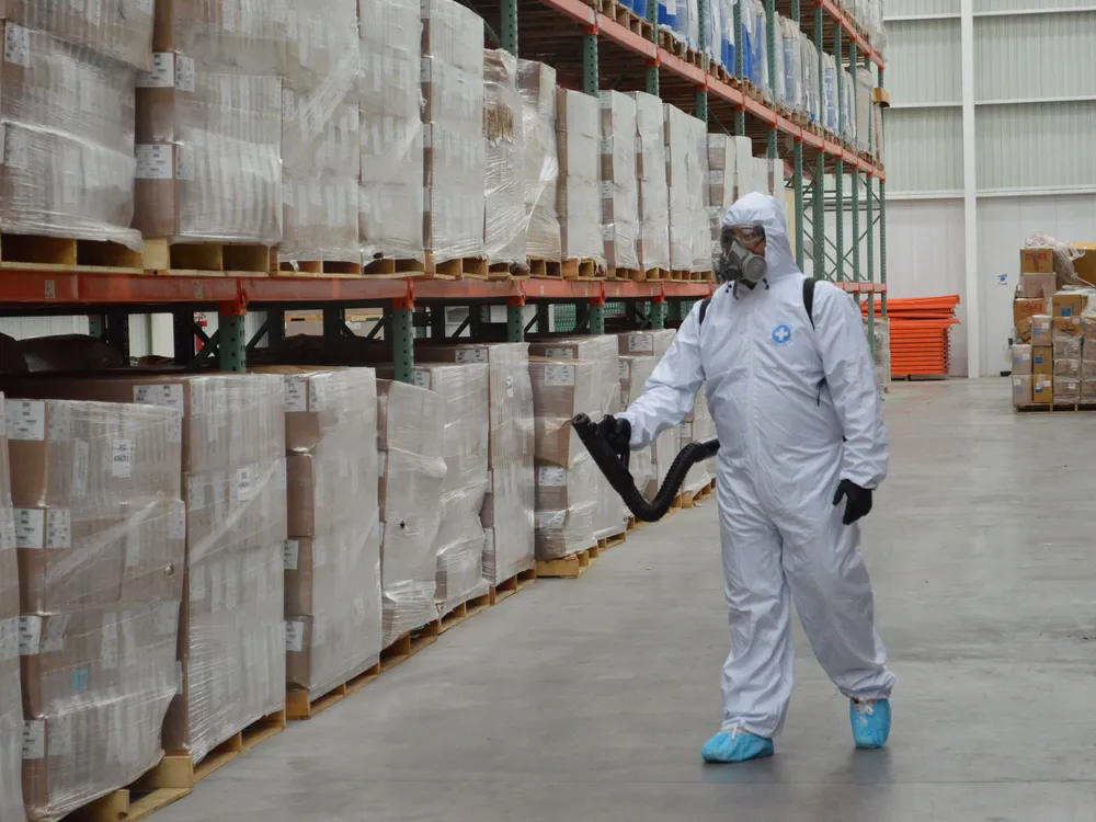 Técnico con equipo de sanitización caminando entre racks de un almacén